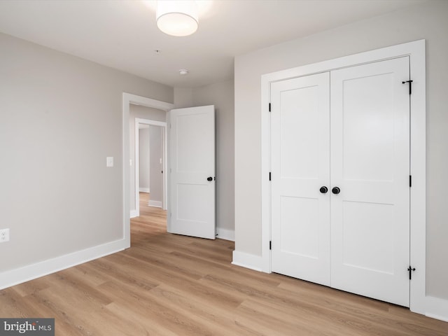 unfurnished bedroom with light wood-type flooring, baseboards, and a closet