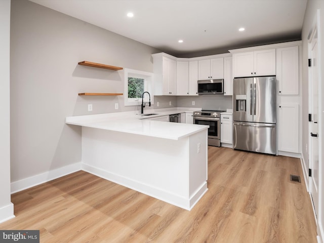 kitchen featuring a peninsula, a sink, visible vents, light countertops, and appliances with stainless steel finishes