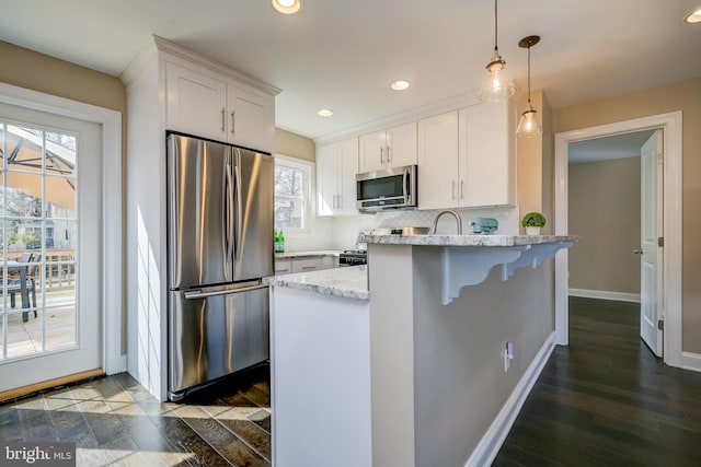 kitchen featuring backsplash, light stone countertops, appliances with stainless steel finishes, a peninsula, and white cabinets