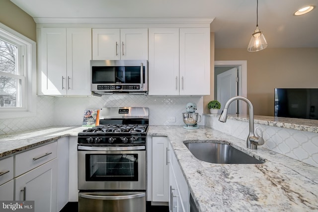 kitchen with light stone counters, a sink, white cabinets, appliances with stainless steel finishes, and backsplash