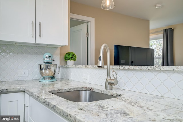 kitchen with a sink, light stone counters, tasteful backsplash, and white cabinets