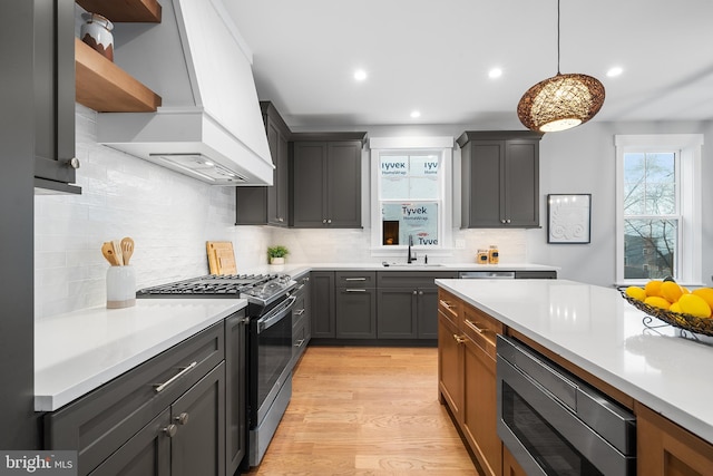 kitchen with stainless steel appliances, light wood-type flooring, light countertops, and custom range hood