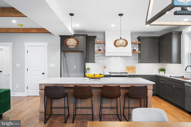 kitchen with a sink, light countertops, light wood-type flooring, open shelves, and backsplash