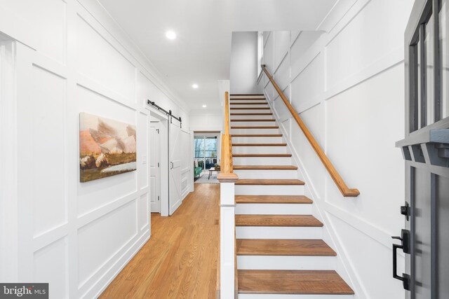 stairway featuring recessed lighting, wood finished floors, a decorative wall, and a barn door