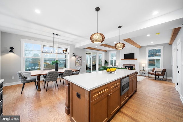 kitchen featuring light countertops, open floor plan, a kitchen island, light wood-type flooring, and a warm lit fireplace