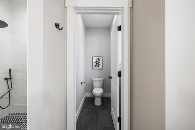 full bath featuring tiled shower, toilet, and baseboards