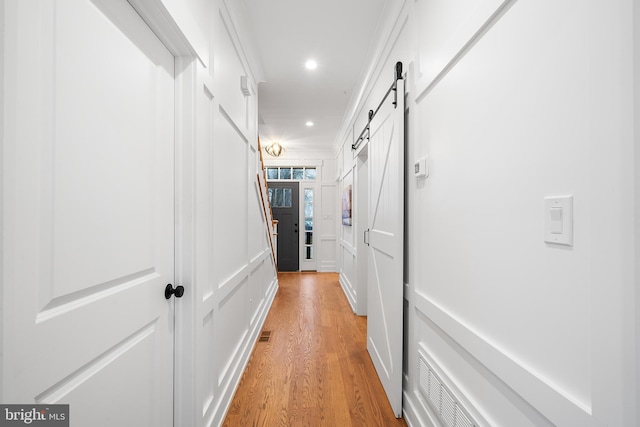 hall with a barn door, crown molding, light wood-type flooring, a decorative wall, and recessed lighting