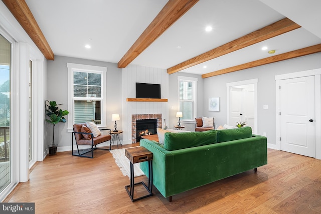 living area with light wood finished floors, beamed ceiling, a fireplace, and baseboards