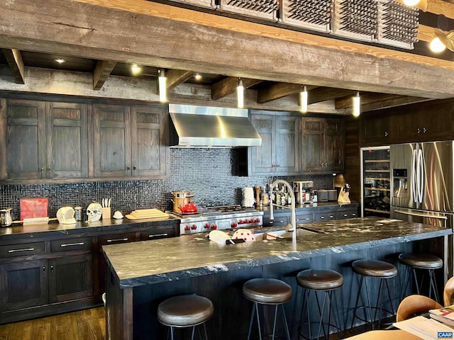 kitchen featuring a kitchen bar, beamed ceiling, backsplash, and wall chimney exhaust hood