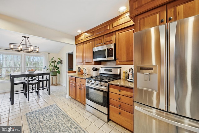 kitchen featuring light stone countertops, light tile patterned flooring, appliances with stainless steel finishes, brown cabinets, and a chandelier