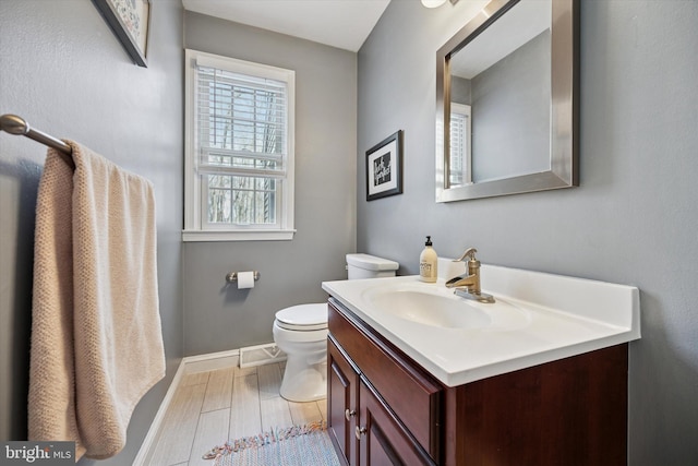 half bath with vanity, toilet, wood finished floors, and baseboards