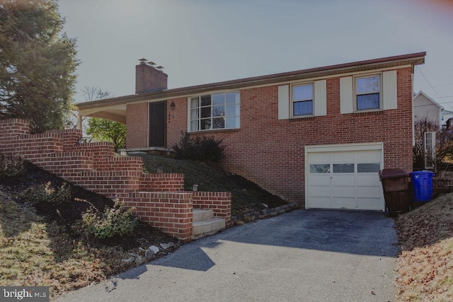 ranch-style house featuring a chimney, brick siding, an attached garage, and driveway