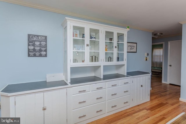 interior space with glass insert cabinets, white cabinets, crown molding, and light wood finished floors