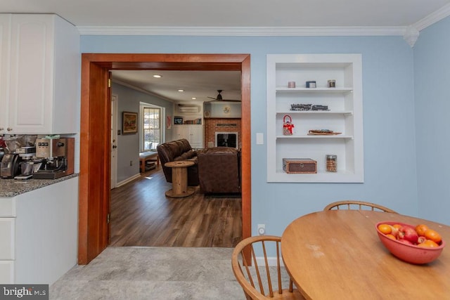 dining space featuring crown molding, built in shelves, a fireplace, and wood finished floors