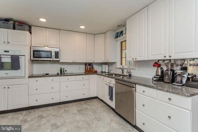 kitchen featuring white cabinetry, dark stone counters, appliances with stainless steel finishes, and a sink