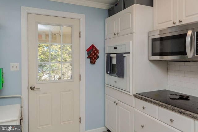 kitchen with oven, stainless steel microwave, white cabinetry, decorative backsplash, and black electric stovetop