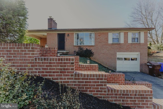 single story home featuring a chimney, brick siding, an attached garage, and driveway