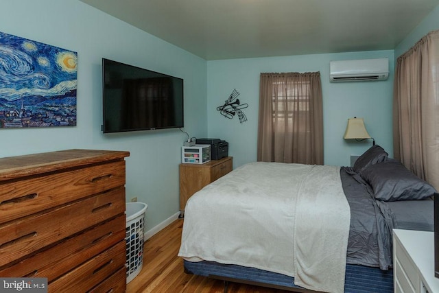 bedroom featuring a wall unit AC, wood finished floors, and baseboards