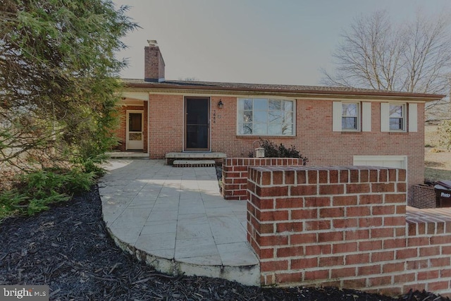 view of front of house featuring a patio, brick siding, and a chimney