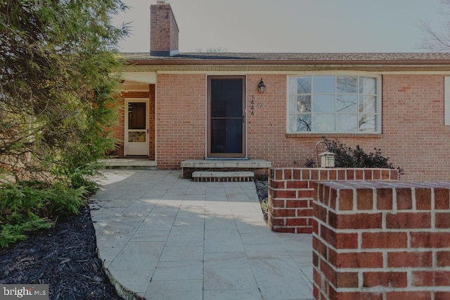 entrance to property with brick siding, a chimney, and a patio area