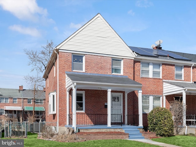 view of front of house with a porch, fence, brick siding, and roof mounted solar panels