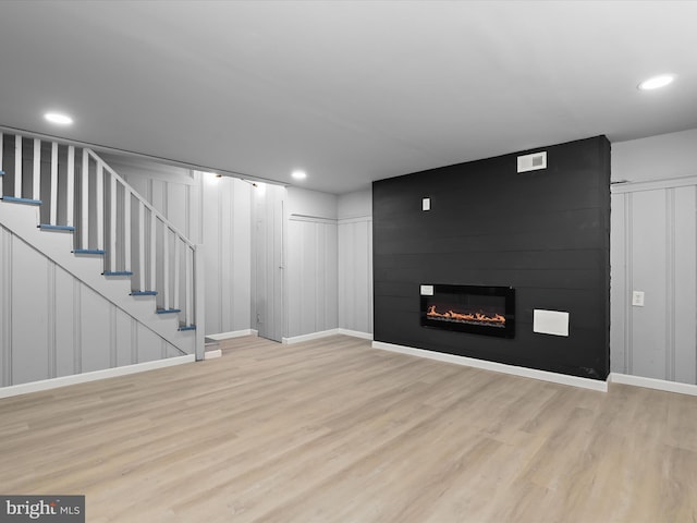 below grade area with wood finished floors, recessed lighting, stairway, a large fireplace, and baseboards