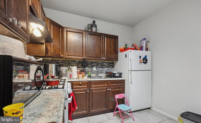 kitchen with tasteful backsplash, freestanding refrigerator, light countertops, under cabinet range hood, and a sink