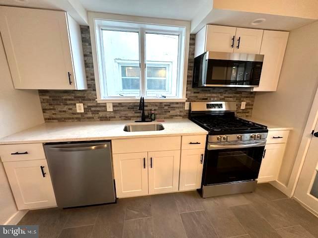 kitchen featuring stainless steel appliances, white cabinetry, a sink, and tasteful backsplash