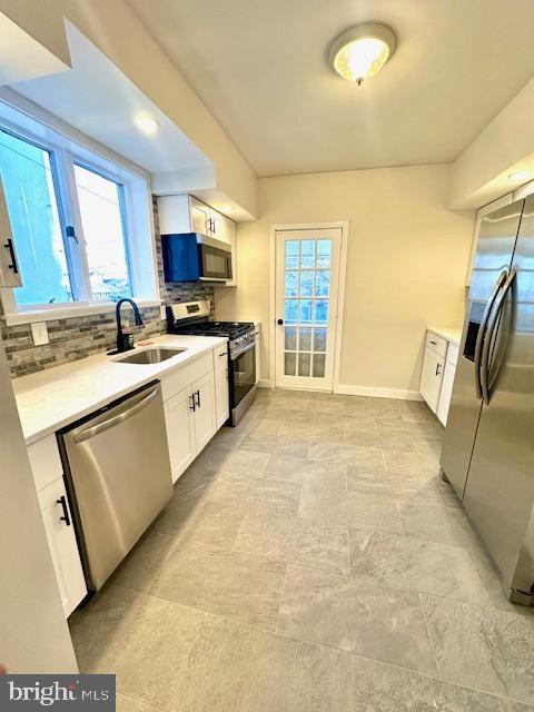 kitchen with a sink, white cabinets, light countertops, appliances with stainless steel finishes, and backsplash