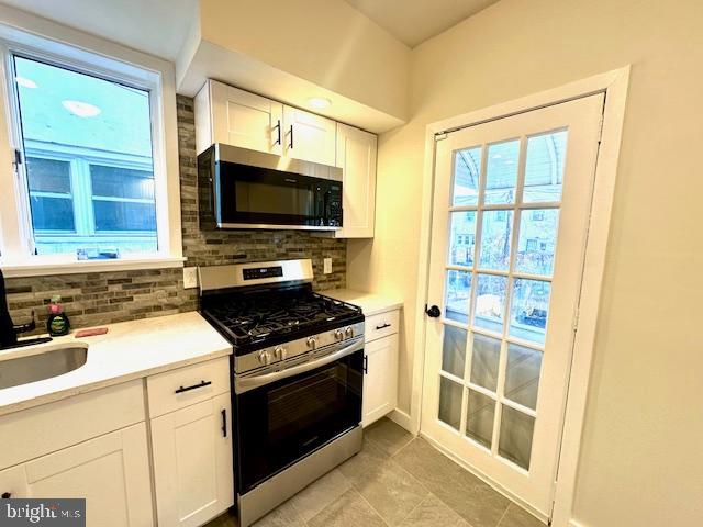 kitchen with light countertops, decorative backsplash, appliances with stainless steel finishes, white cabinetry, and a sink