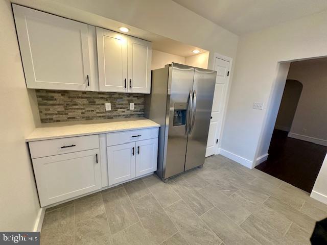 kitchen featuring tasteful backsplash, stainless steel fridge, baseboards, light countertops, and white cabinetry