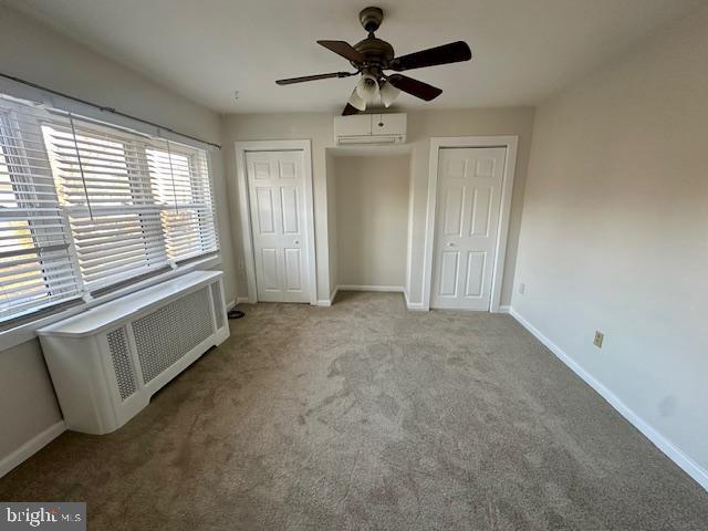 unfurnished bedroom featuring a wall unit AC, multiple closets, radiator, carpet flooring, and baseboards