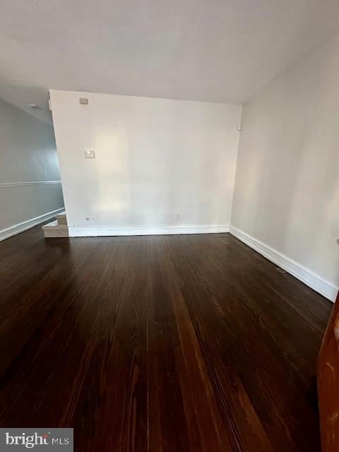 unfurnished room featuring baseboards and dark wood-type flooring