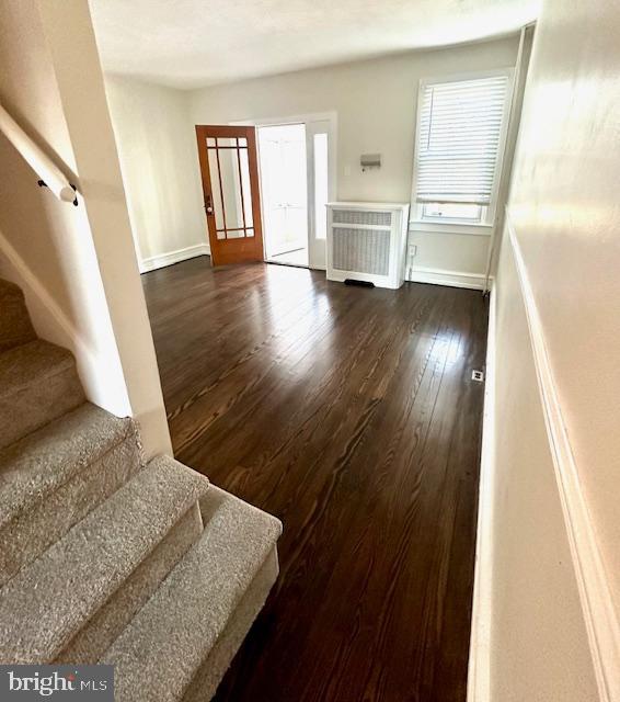 entrance foyer featuring dark wood-style floors, radiator, stairway, and baseboards