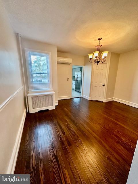 unfurnished room with baseboards, dark wood-style floors, radiator heating unit, an inviting chandelier, and a wall mounted AC