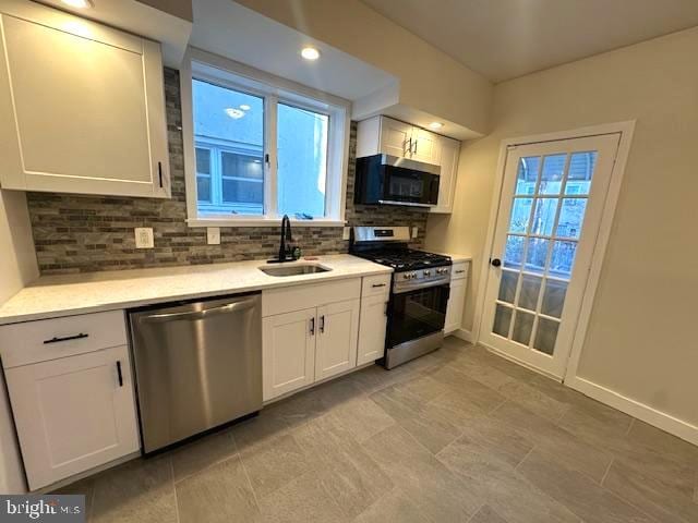 kitchen with tasteful backsplash, appliances with stainless steel finishes, a sink, and white cabinets