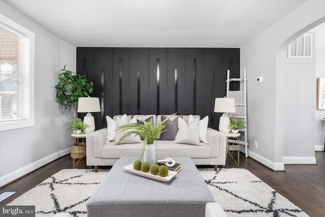 living room with arched walkways, wood finished floors, visible vents, and baseboards