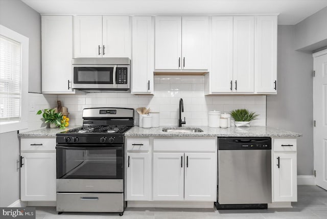 kitchen featuring stainless steel appliances, a sink, light stone countertops, and white cabinets