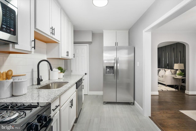 kitchen with arched walkways, appliances with stainless steel finishes, white cabinets, a sink, and light stone countertops