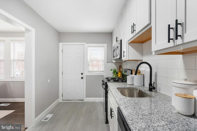 kitchen with light stone counters, black gas range, a sink, backsplash, and stainless steel microwave