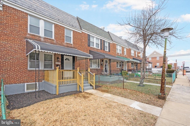 multi unit property with mansard roof, brick siding, a shingled roof, fence, and a residential view