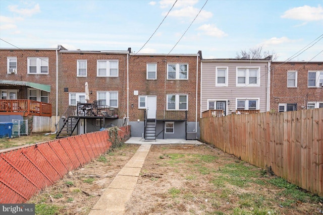 rear view of house featuring brick siding, stairway, central AC unit, and a fenced backyard