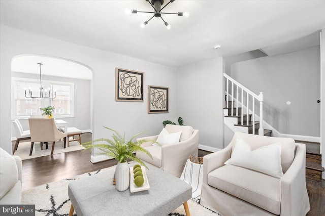 living area with baseboards, arched walkways, wood finished floors, an inviting chandelier, and stairs