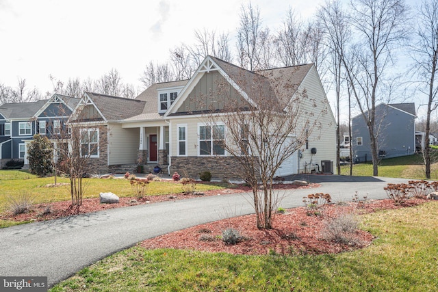 craftsman-style house featuring stone siding, a garage, driveway, and a front lawn