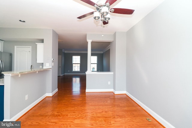 interior space featuring decorative columns, a ceiling fan, ornamental molding, light wood-type flooring, and baseboards