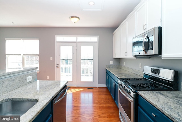 kitchen with blue cabinets, appliances with stainless steel finishes, and white cabinets