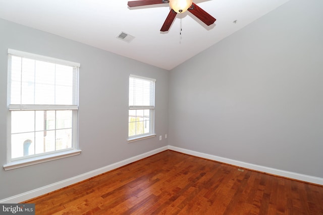 empty room with visible vents, vaulted ceiling, baseboards, and wood finished floors