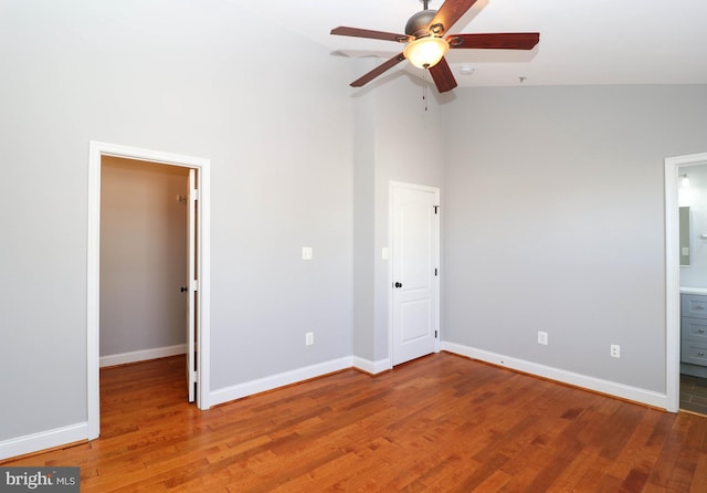 unfurnished bedroom with a walk in closet, connected bathroom, baseboards, and wood finished floors