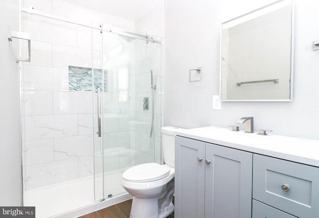 full bathroom featuring wood finished floors, a stall shower, vanity, and toilet