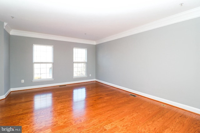 empty room with visible vents, baseboards, wood finished floors, and ornamental molding